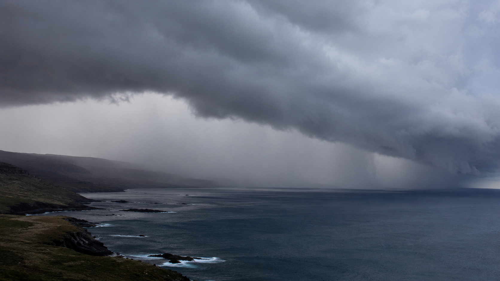 Bande de nuages bas et rideaux de pluie avançant depuis la mer sur un littoral rocheux