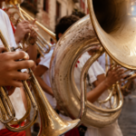 Des mains jeunes tiennent une trompette et le pavillon d'un soubassophone dans une rue ensoleillée en fête