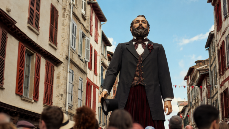 Un géant de procession représentant un homme barbu en redingote, porté au-dessus de la foule dans une rue de vieille ville