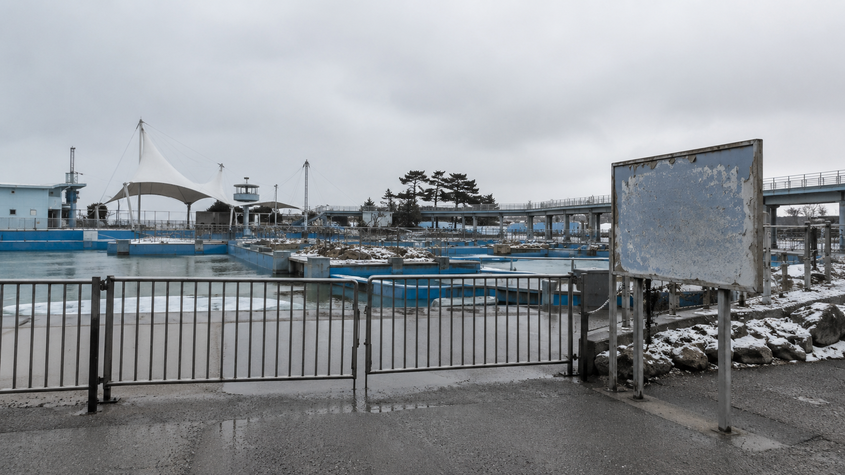 Un parc marin désert en hiver, clôture fermée et bassins de spectacle vides sous un ciel gris