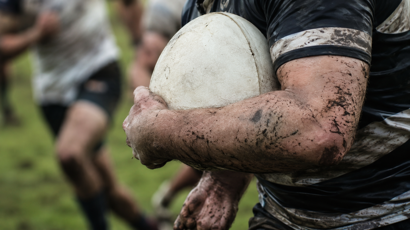 Gros plan sur un ballon de rugby serré contre le torse d'un joueur lors d'une percée de fin de match
