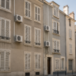Plusieurs unités de climatisation split blanches fixées sur la façade d'un immeuble d'habitation, volets fermés