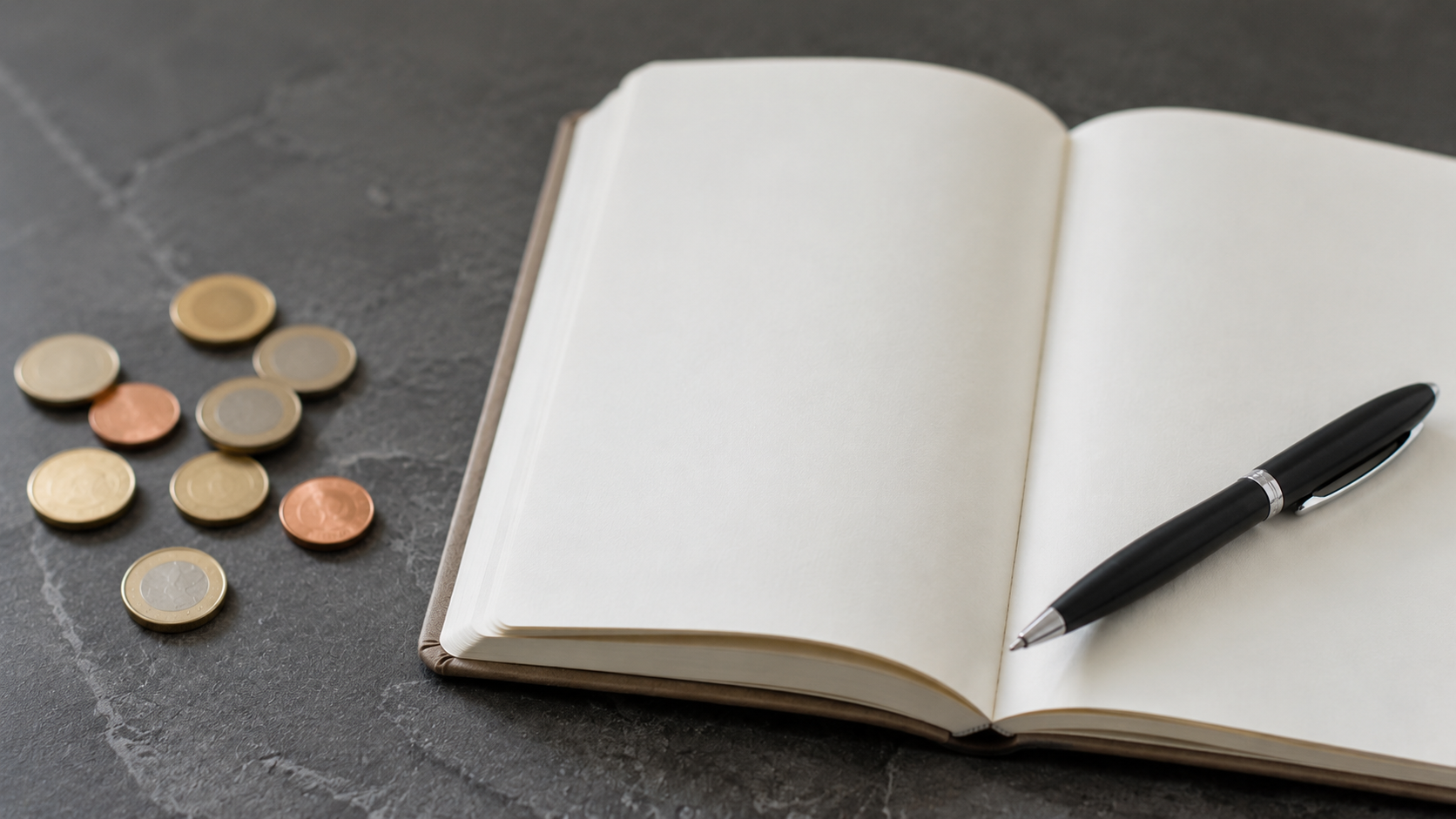 Quelques pièces en euros posées à côté d'un carnet ouvert et d'un stylo sur une table