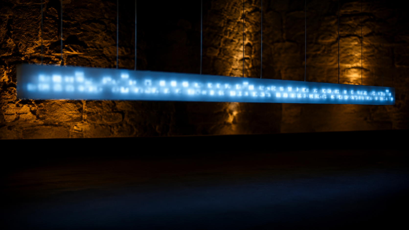 Un bandeau lumineux flou au-dessus d'un plateau sombre, évoquant un écran de surtitres devant un mur de pierre