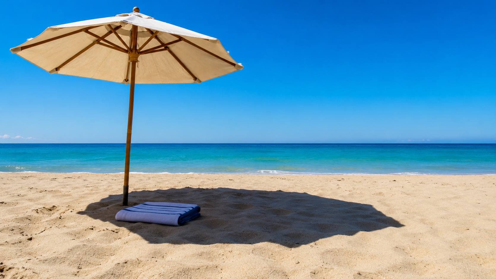 Parasol de plage et serviette pliee projetant de l'ombre sur le sable sous un ciel bleu