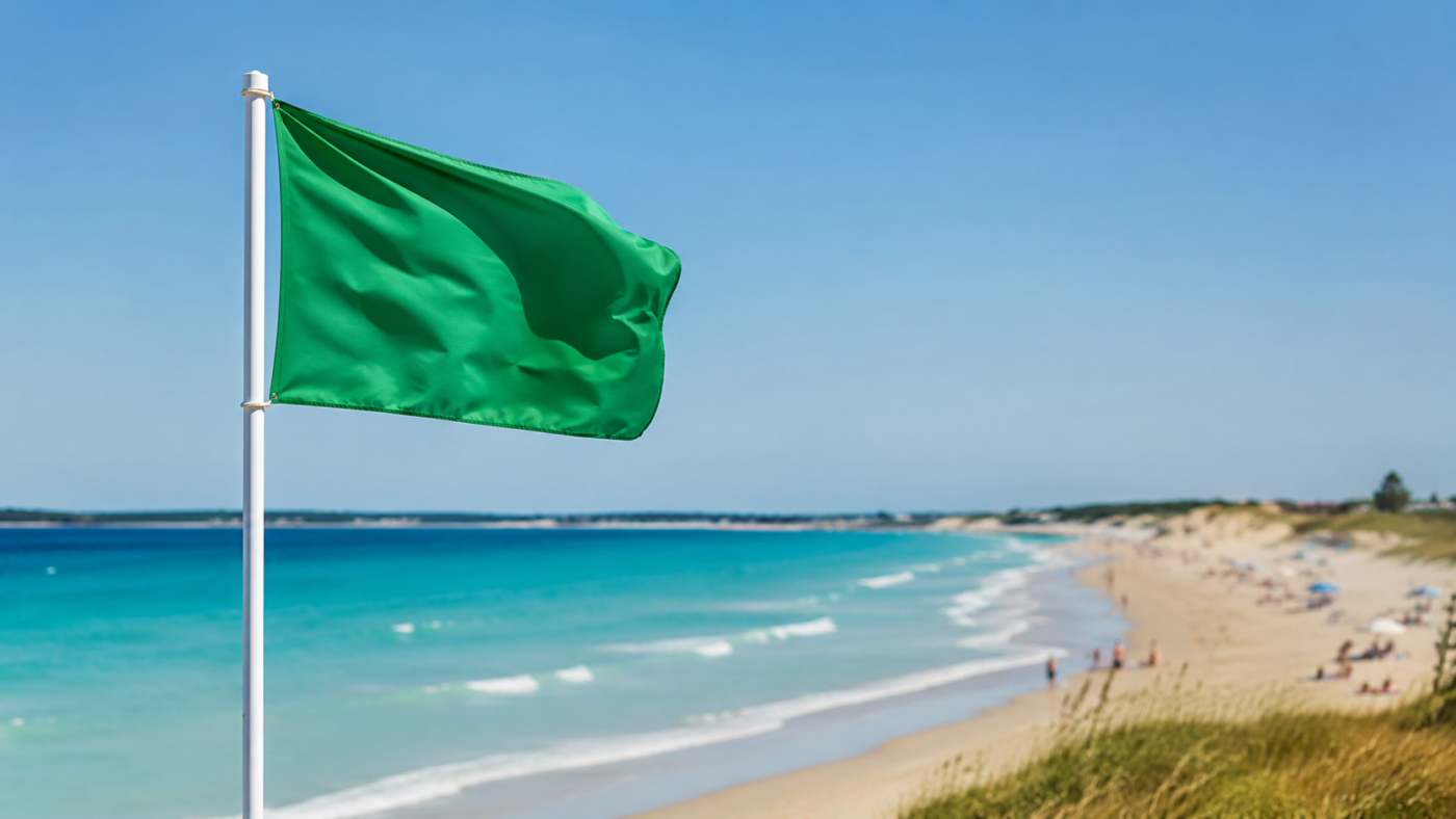 Plage française en été avec un drapeau de poste de secours au premier plan et une mer claire