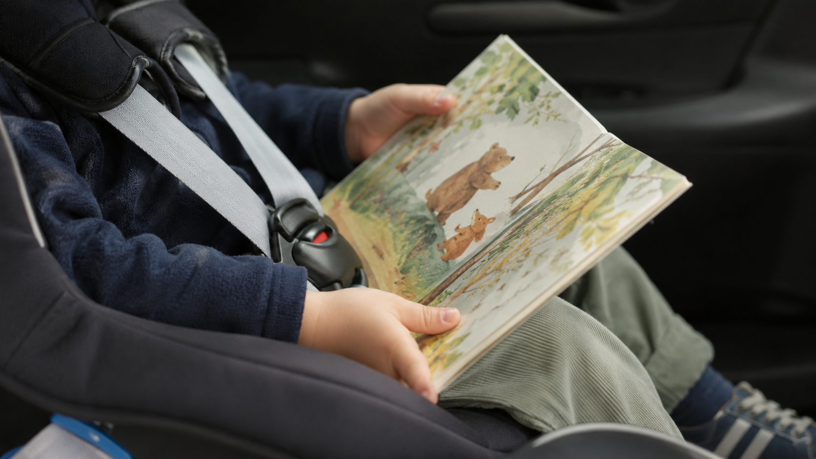 Mains d'un jeune enfant tenant un livre illustré sur ses genoux dans une voiture