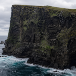 Falaise de basalte sombre d'une petite île atlantique tombant droit dans la mer, sans quai ni appontement