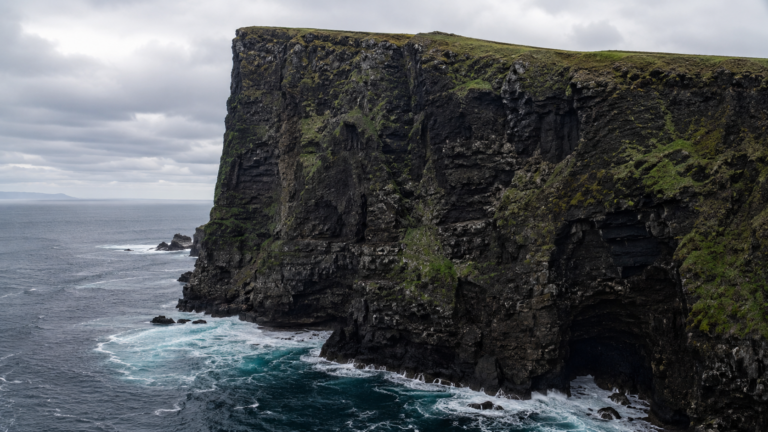 Falaise de basalte sombre d'une petite île atlantique tombant droit dans la mer, sans quai ni appontement