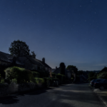 Une rue de village la nuit, lampadaires éteints, éclairée par un clair de lune doux sous un ciel étoilé