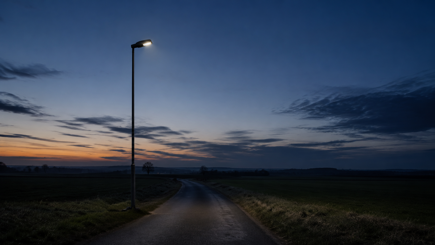 Un lampadaire isolé au bord d'une route de campagne au crépuscule, lumière en train de s'éteindre