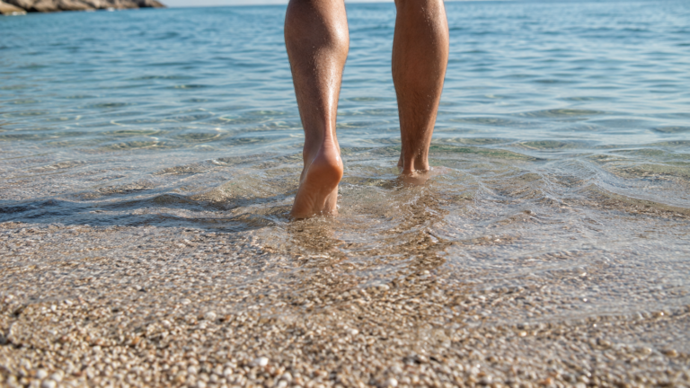 Des pieds nus entrant dans une eau de mer claire et peu profonde au bord du rivage, sous le soleil d'été