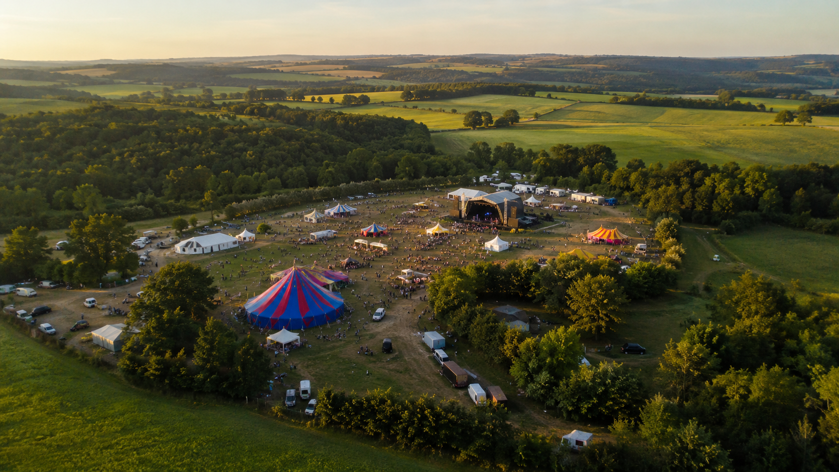 Vue aerienne d'un site de festival de taille moyenne avec des tentes colorees et une scene au milieu de champs verts.