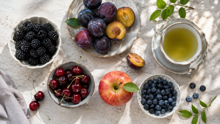 Mûres, prunes, cerises, pomme, myrtilles et une tasse de thé vert sur une table claire