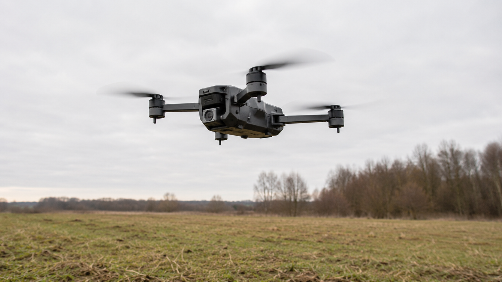 Un petit drone décolle au-dessus d'un champ, hélices en mouvement.