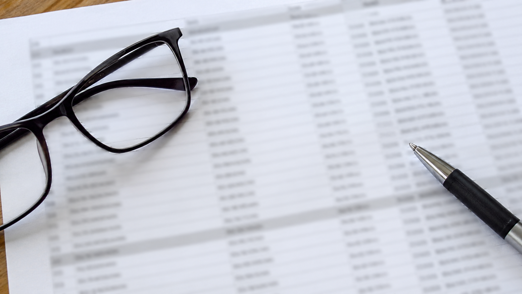 Une liste imprimée de noms posée sur une table, colonnes illisibles, lunettes et stylo à côté