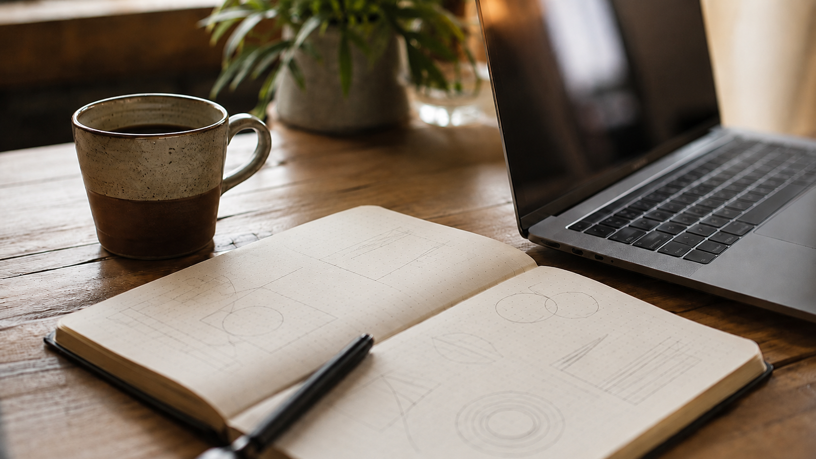 Ordinateur portable ouvert sur un bureau a cote d'un carnet de notes manuscrites floues et d'une tasse de cafe