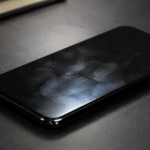 Traces de doigts révélées par une lumière rasante sur l'écran éteint d'un téléphone posé sur un bureau