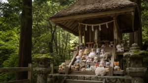 Des peluches génériques alignées comme des offrandes sur les marches d'un petit sanctuaire shinto en bois, en forêt.