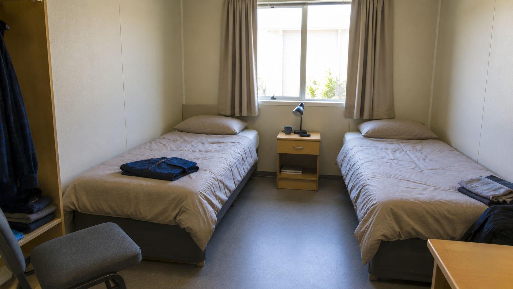 Une chambre-dortoir modeste avec deux lits simples et une petite table de chevet, sans lits superposés