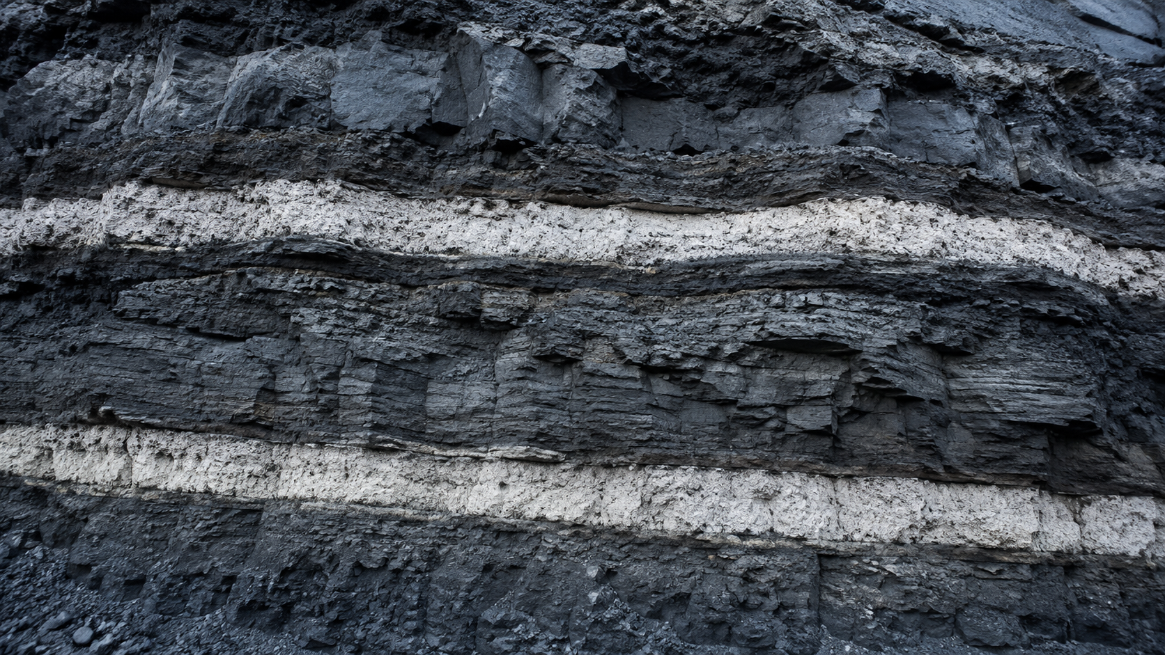 Une paroi rocheuse montrant deux couches claires de cendre volcanique prises dans la roche stratifiee