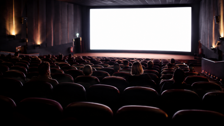 Une salle de cinéma à moitié vide vue des derniers rangs, quelques spectateurs dispersés face à l'écran allumé
