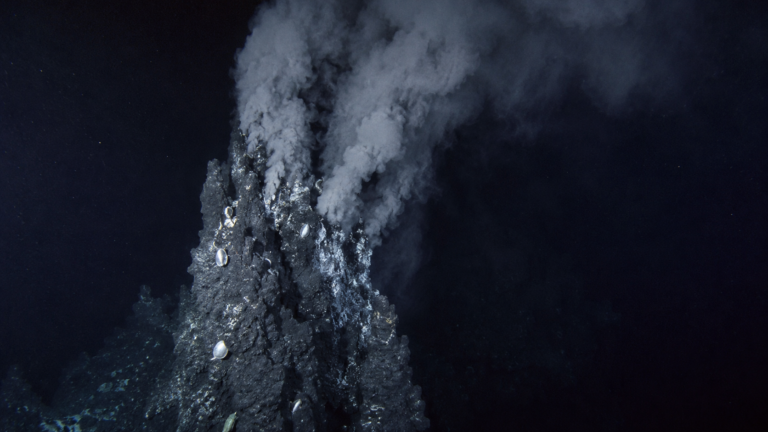 Une cheminée hydrothermale sombre sur le fond de l'océan, éclairée de côté, libérant un panache dans l'eau noire