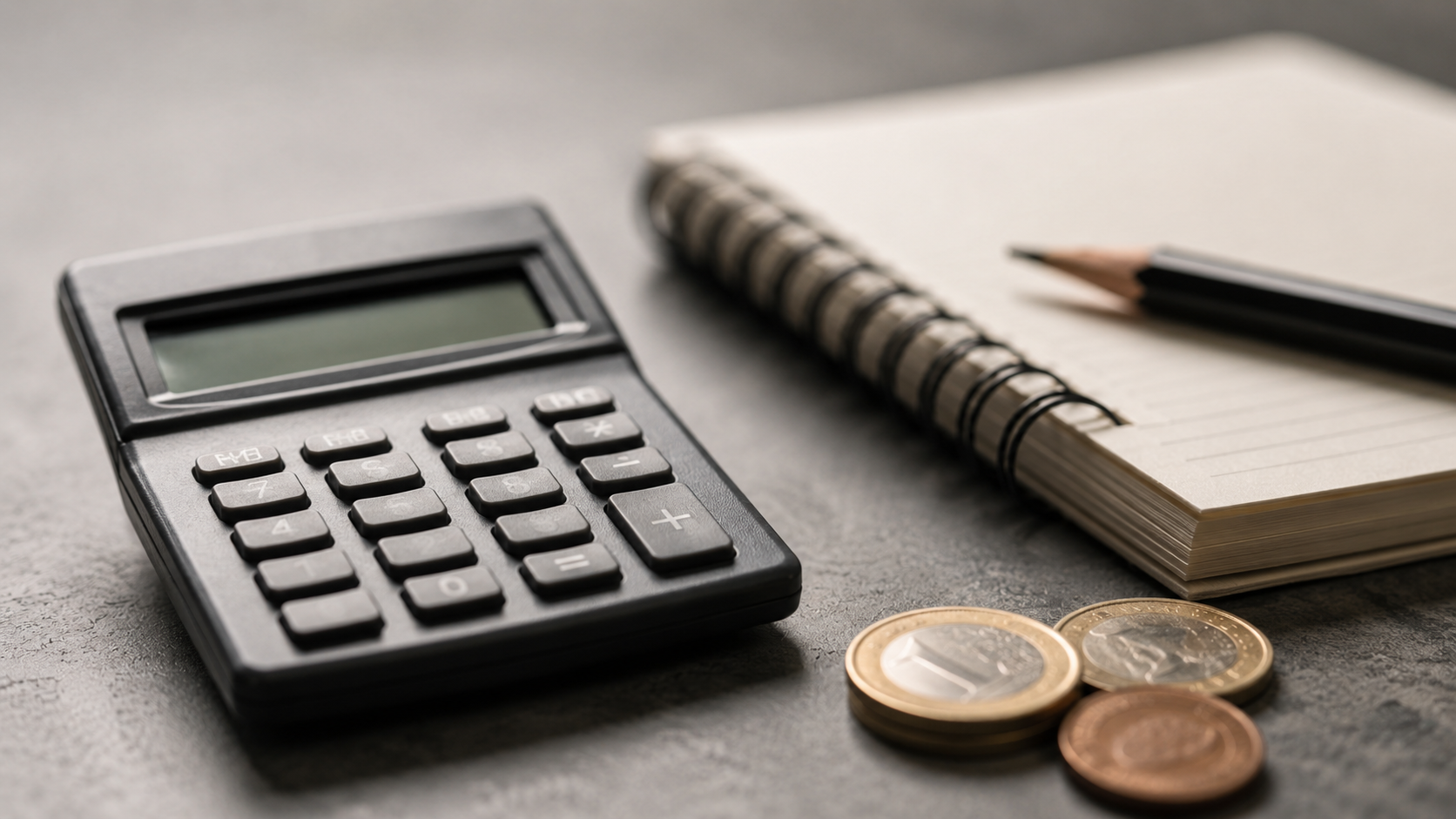 Calculatrice, carnet, crayon et pièces en euros posés sur un bureau.
