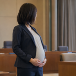 Une femme enceinte en tenue professionnelle dans une salle de mairie, près d'une fenêtre.