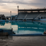 Grand bassin à dauphins vide au crépuscule, gradins gris déserts reflétés dans l'eau turquoise immobile