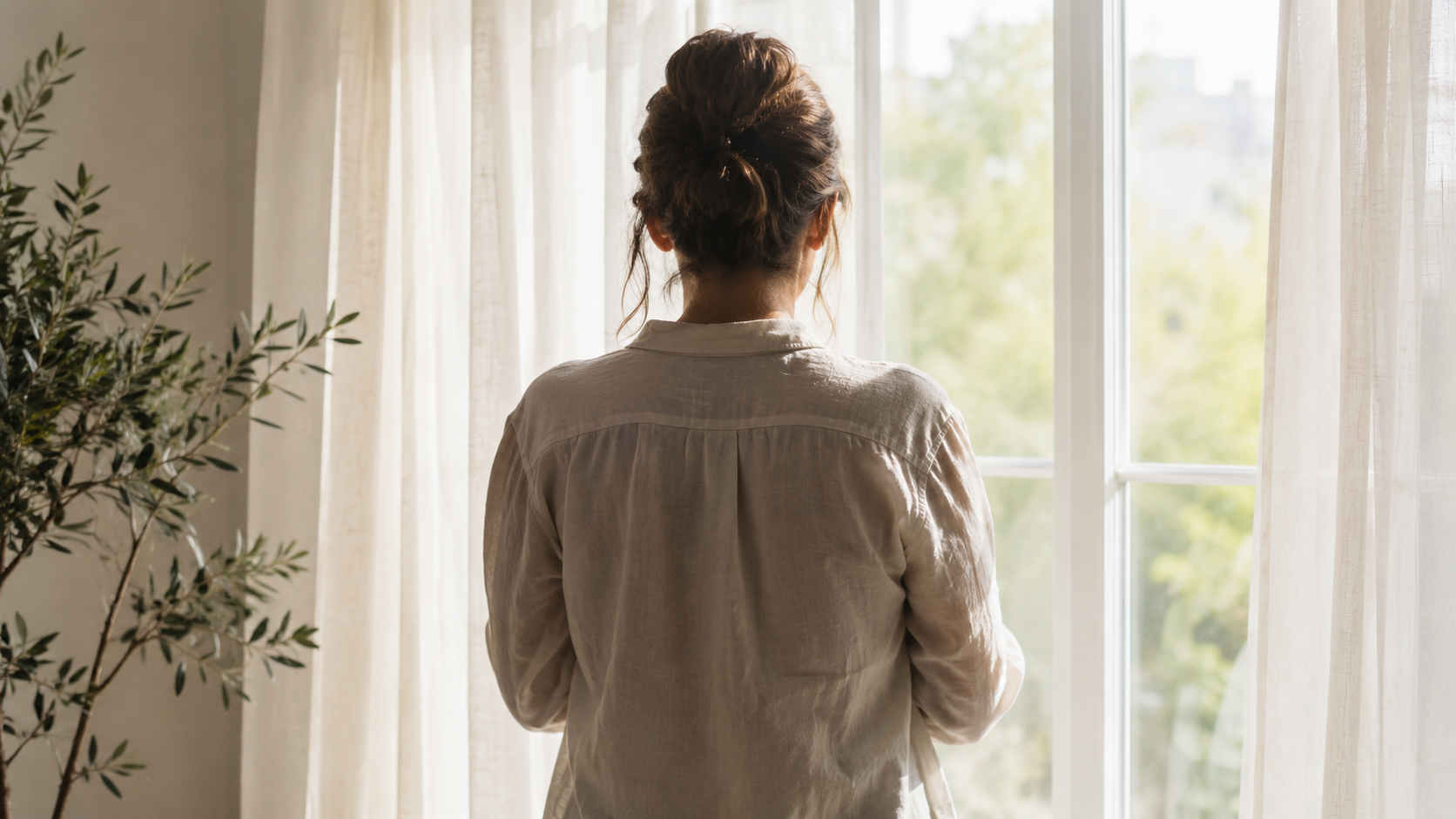Une femme vue de dos devant une fenêtre lumineuse, dans un moment de réflexion