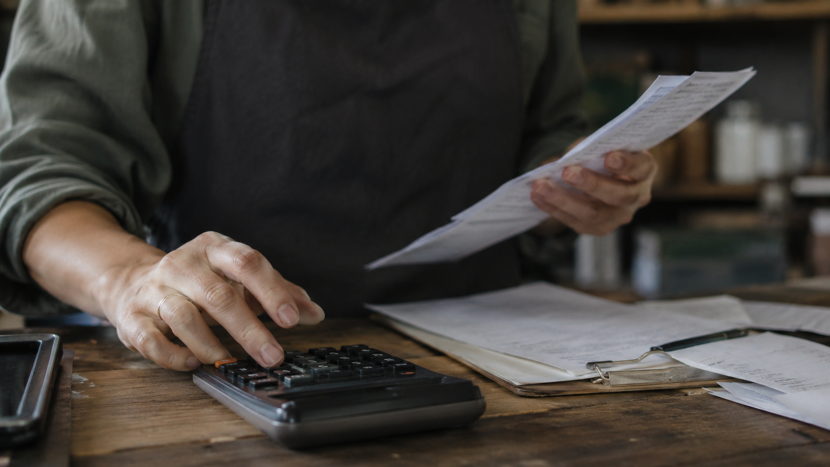 Mains d'un jeune indépendant calculant son budget de cotisations avec une calculatrice