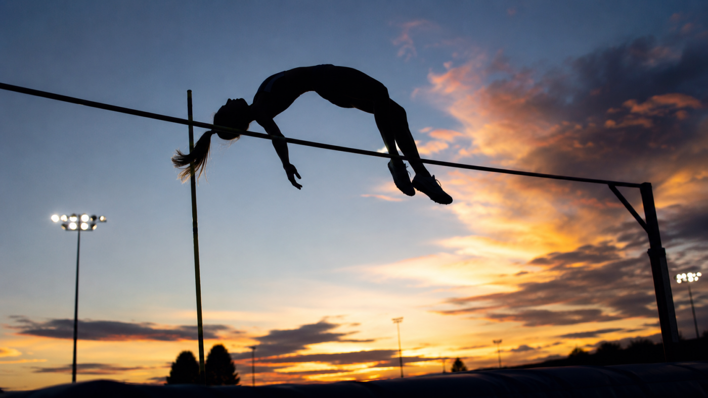 Perchiste feminine generique en silhouette a contre-jour franchissant la barre au sommet du saut, ciel du soir