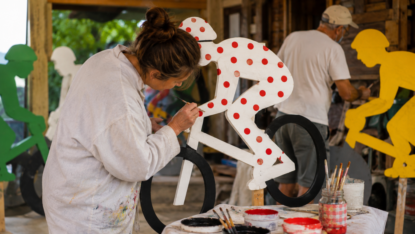 Des bénévoles peignent des silhouettes de cyclistes en bois dans un atelier de village