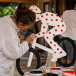 Des bénévoles peignent des silhouettes de cyclistes en bois dans un atelier de village