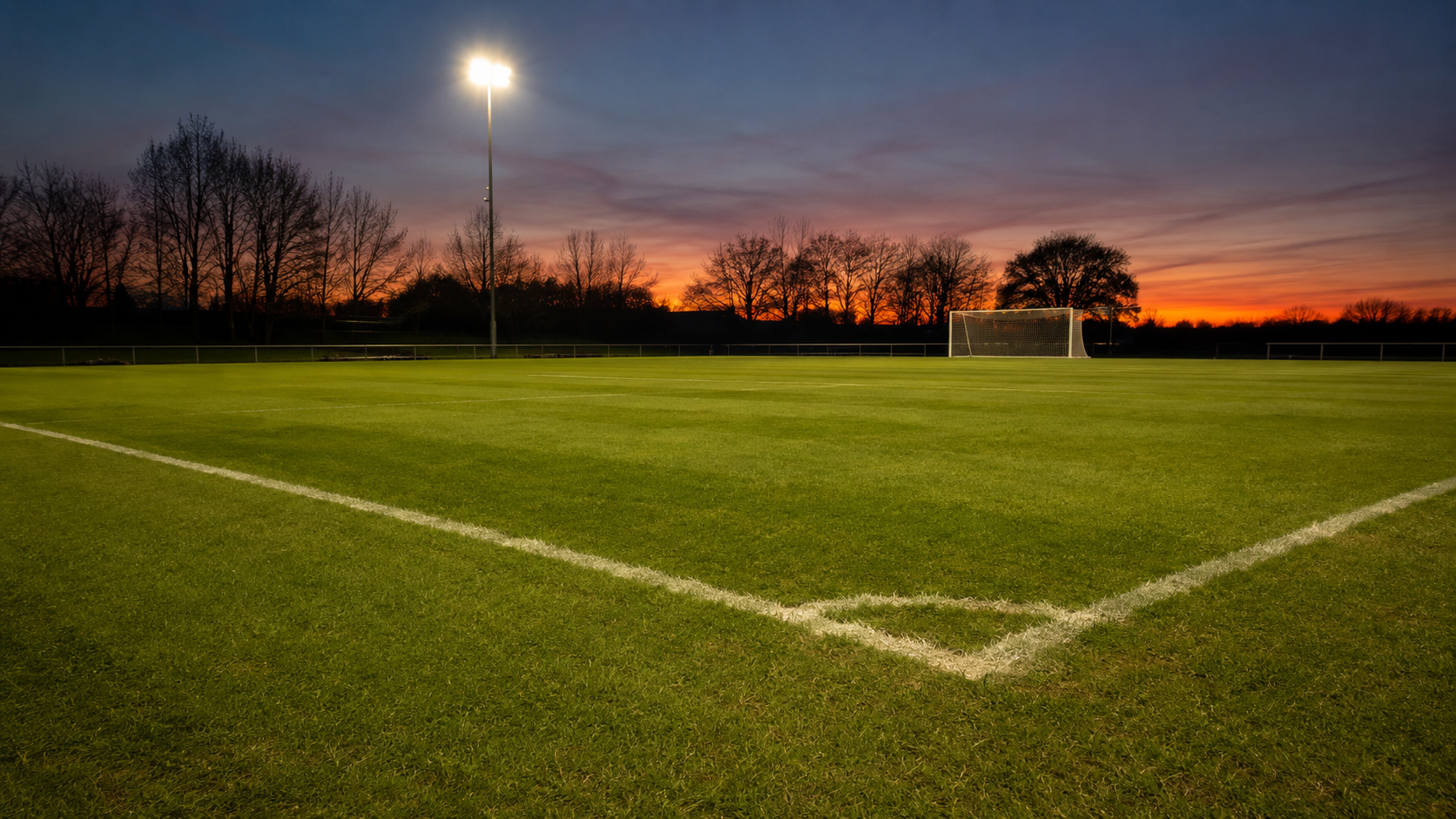 Une pelouse de stade de football vide au crépuscule, avec une cage et son filet au fond.