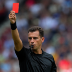 Un arbitre générique brandit un carton rouge sur une pelouse, foule floue en arrière-plan