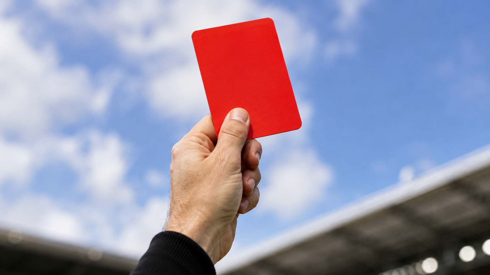 Gros plan sur une main d'arbitre générique tenant un carton rouge levé vers le ciel