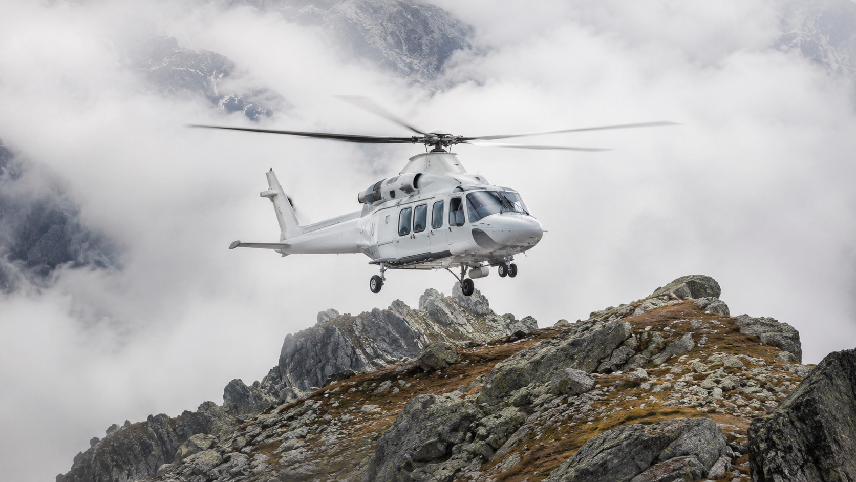 Hélicoptère de secours sans marquage en vol stationnaire au-dessus d'une crête rocheuse dans la brume, terrain de haute montagne