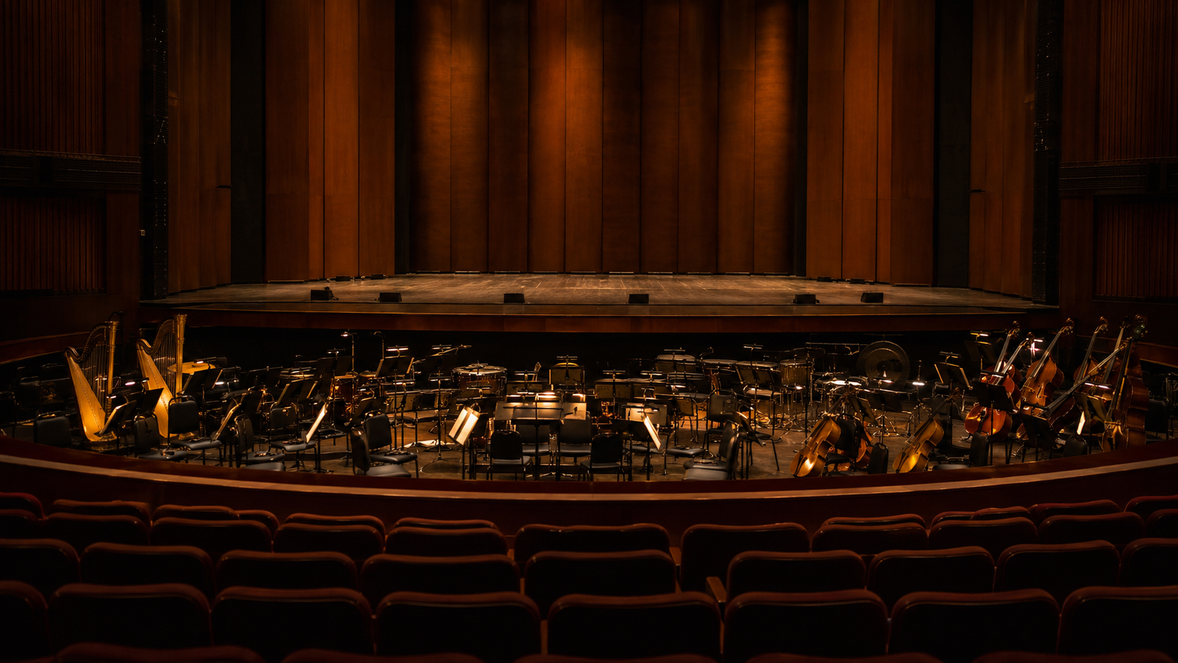 Une fosse d'orchestre éclairée vue du fond d'une salle de concert vide, pupitres et instruments en place