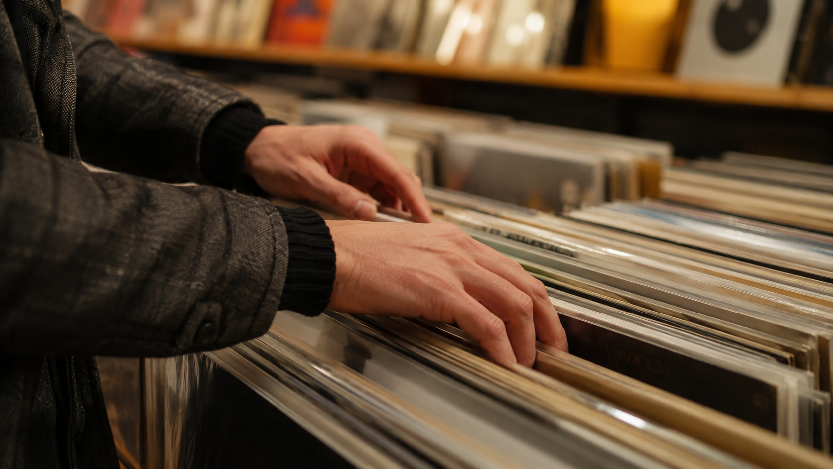 Des mains feuilletant des vinyles dans un bac de disquaire, rangées de pochettes en arrière-plan