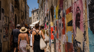 Une rue étroite couverte d'affiches de théâtre superposées, des festivaliers marchant de dos en plein soleil
