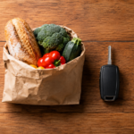 Vue de dessus d'une table de cuisine en bois où sont alignés un trousseau de clés, un sac en papier avec du pain et des légumes, une clé de voiture et un robinet de radiateur