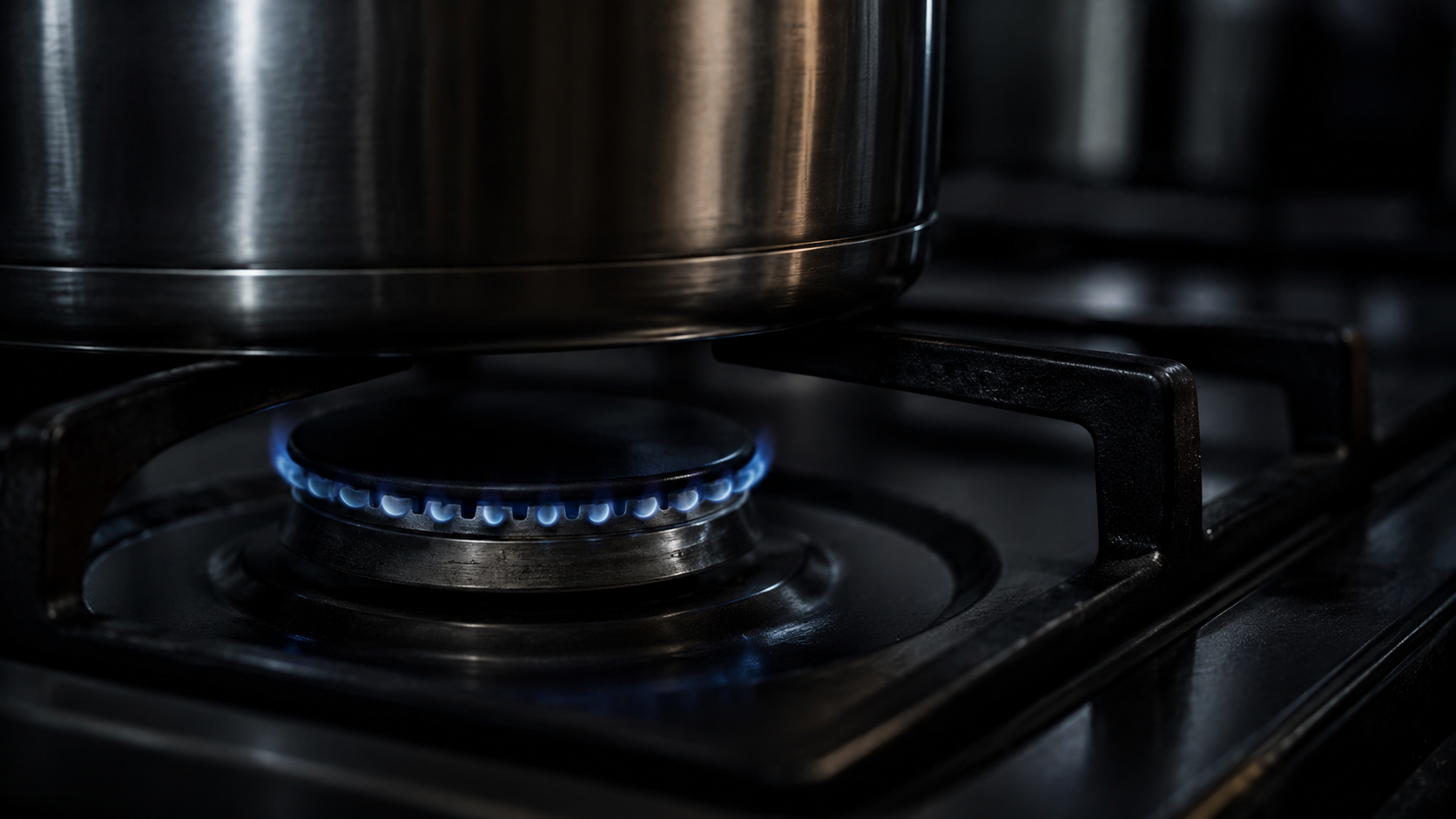 Gros plan d'un brûleur à gaz réglé au minimum, couronne de flamme bleue dans une cuisine sombre, casserole en acier posée à côté