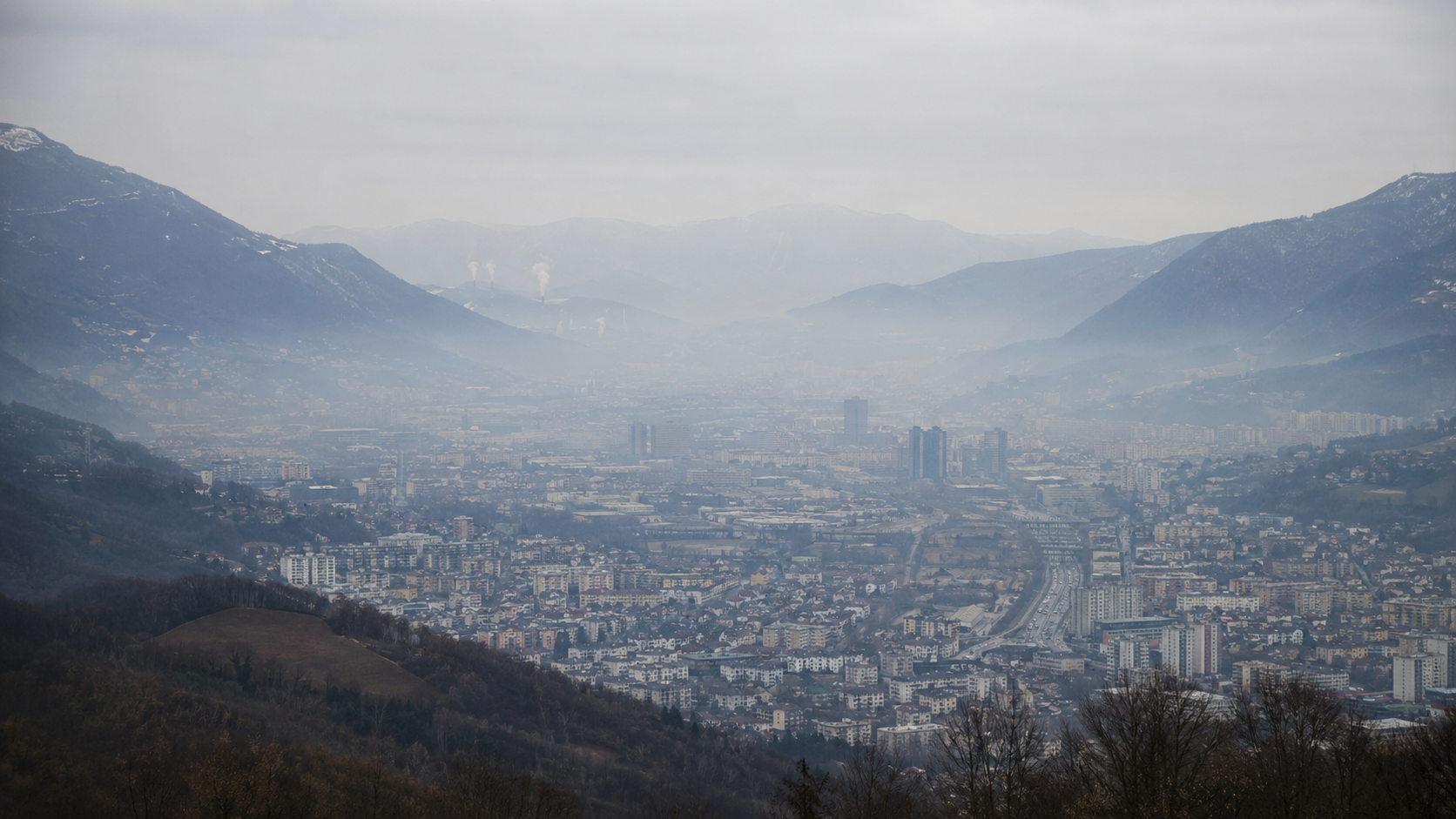 Une vallée urbaine européenne sous une légère brume hivernale piégée entre les reliefs