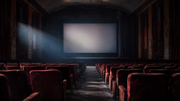 Salle de cinéma vide et sombre, fauteuils de velours rouge face à un écran éteint