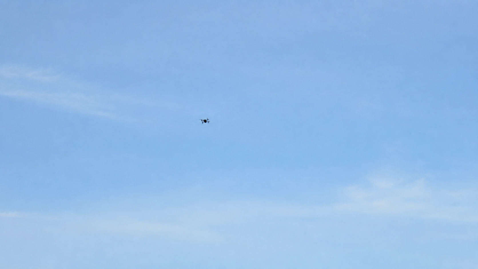 Petit drone quadricoptère vu de loin dans un ciel dégagé