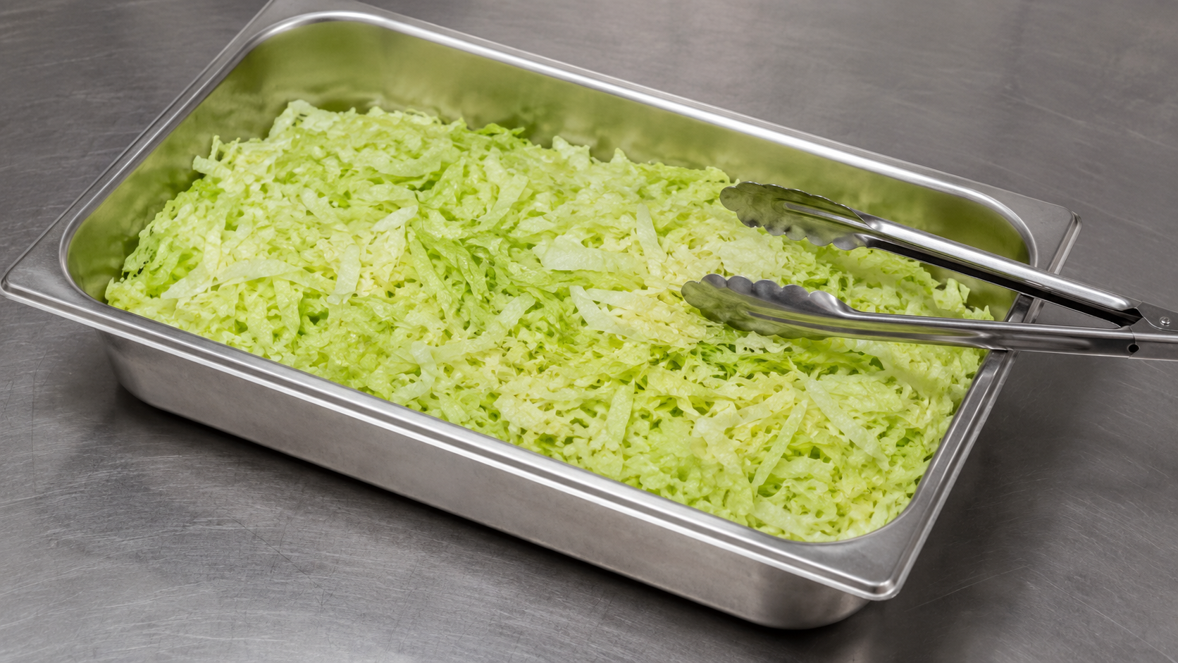 Bac de laitue iceberg finement râpée sur un plan de travail inox de cuisine professionnelle