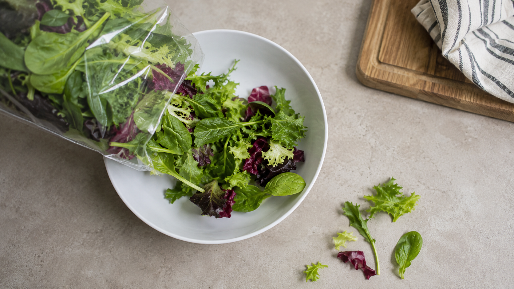Des feuilles de salade versées d'un sachet transparent neutre dans un saladier blanc
