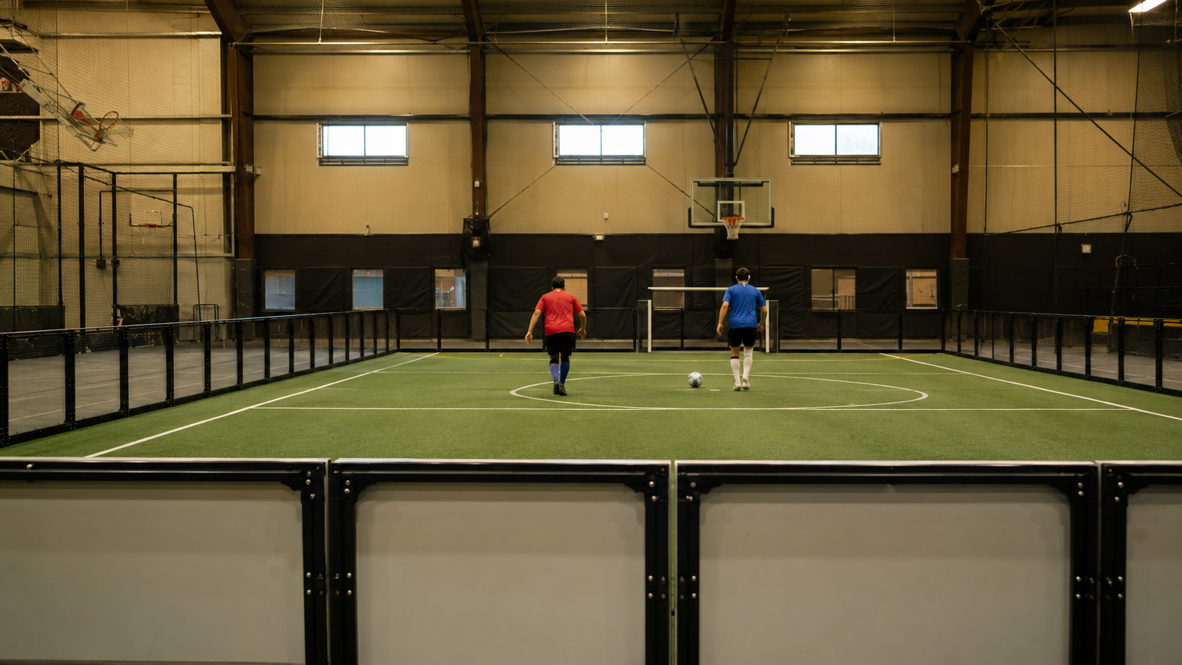 Gymnase avec un terrain bordé de barrières, deux joueurs anonymes de dos avec bandeaux